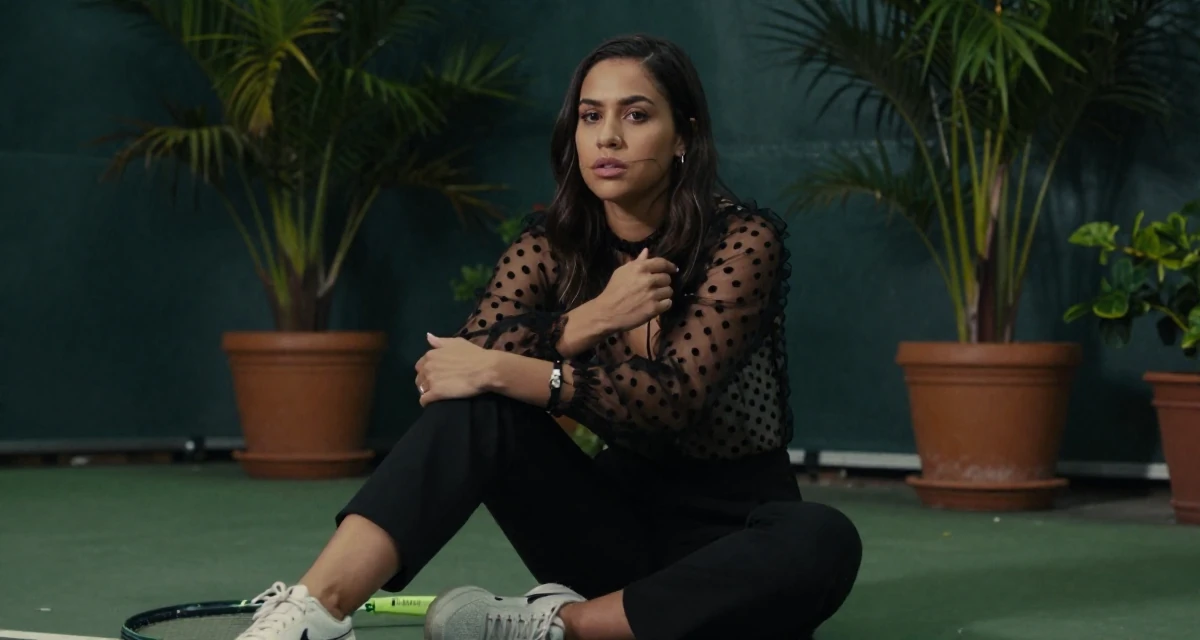 A indifferent Female From Bahamas, studied finance and banking in their 25, handling first DMs from subscribers respectfully, wearing a sheer polka dot blouse and black trousers, gripping a lapel in a tennis court.