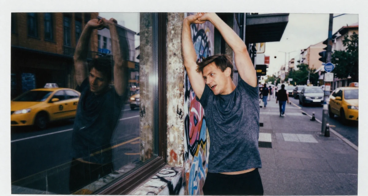 A passionate male Born in Ukraine, majored in creative communication in their 26, working through back-to-back burnout cycles, wearing a sporty athleisure look, checking a reflection in a window in a graffiti art wall.