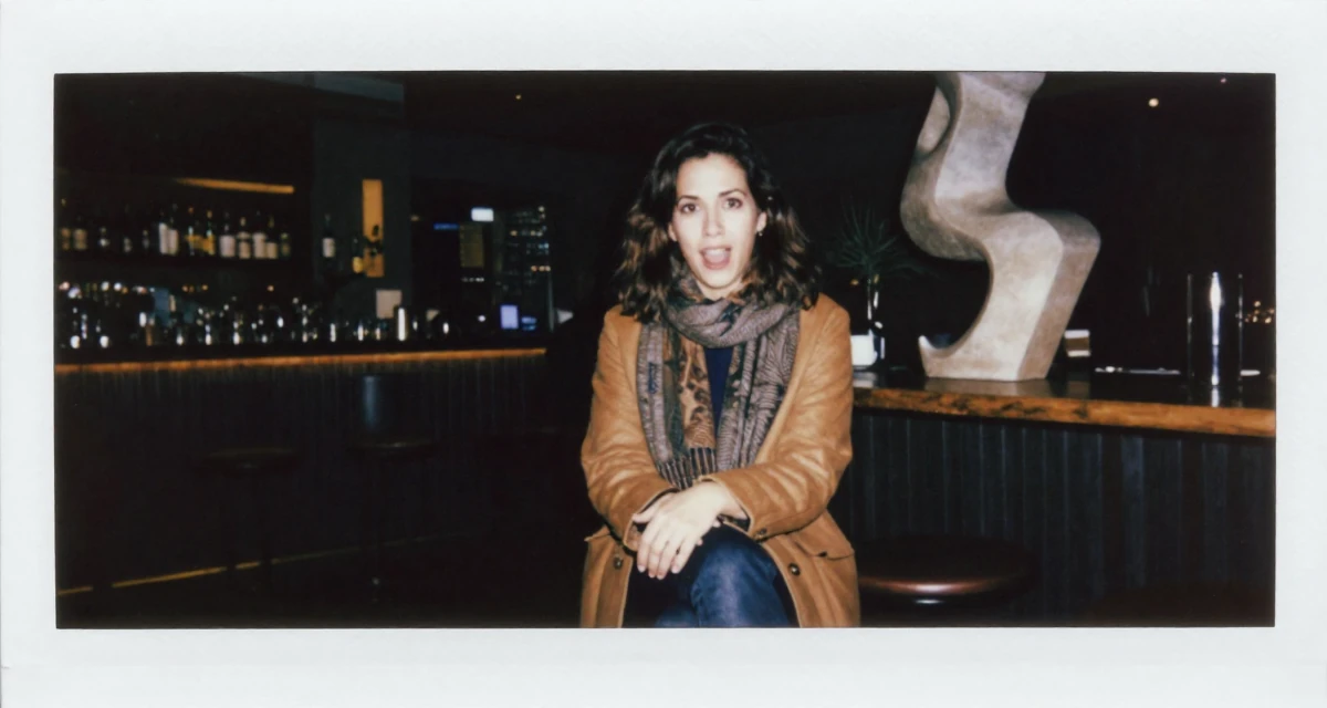 A anxious but excited Female From Panama, majored in media production in their 37, trying to stabilize income streams, wearing a layered autumn coat and scarf, crossing legs in a dimly lit jazz bar.