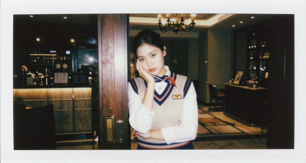 A inspired Female Former hotel concierge, now offering luxury-inspired lifestyle content in their 25, dealing with anxiety about first paying subscribers, wearing a preppy sweater vest combo, leaning against a door in a hotel lobby.