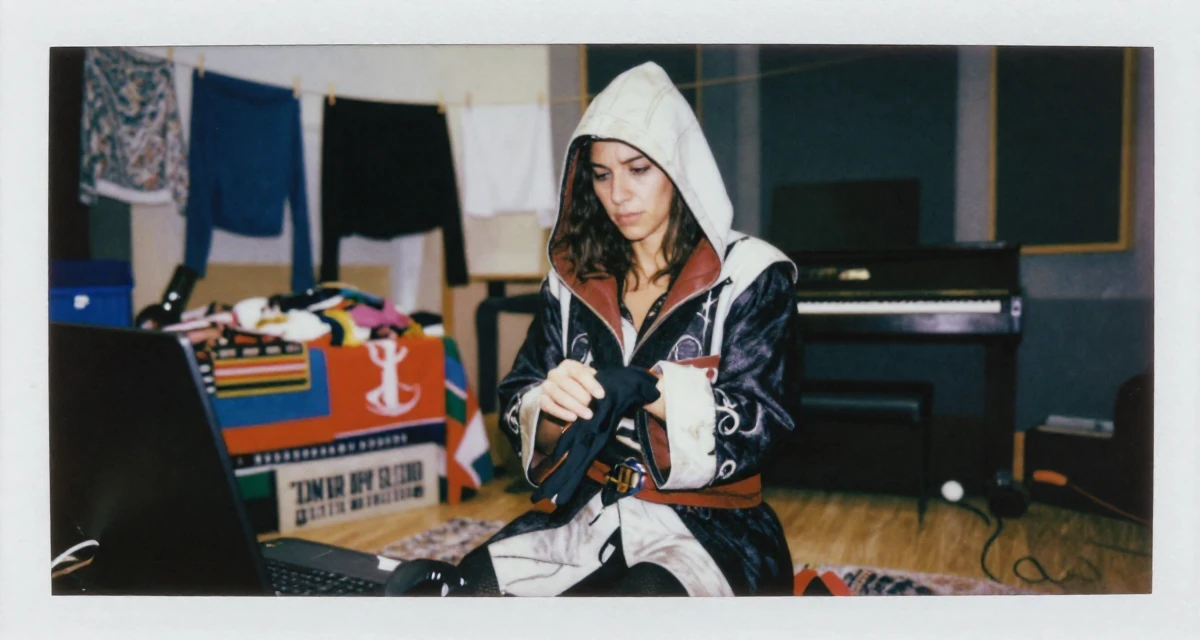 A stressed Female From Israel, studied behavioral economics in their 32, building a side hustle while working full-time, wearing a assassin creed style hooded robe and tunic, removing a glove in a music studio.