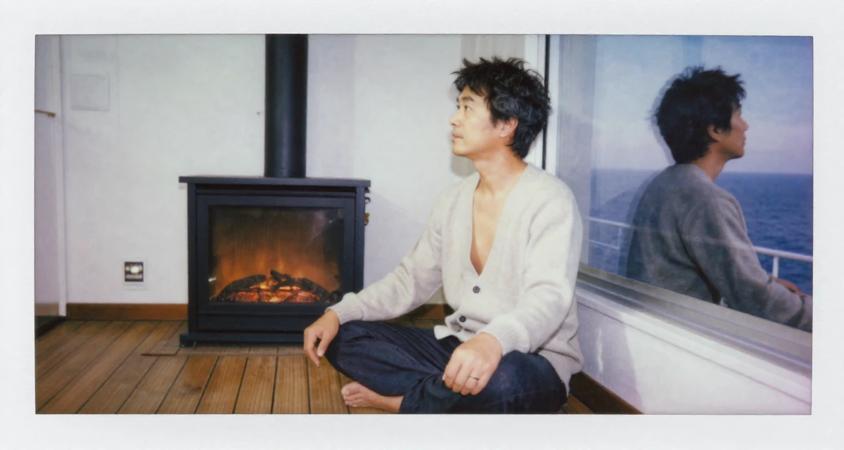 A relaxed male From Japan, majored in animation in their 51, switching careers later in life, wearing a open-back sweater showing the spine, looking at a reflection in a window in a ferry deck.