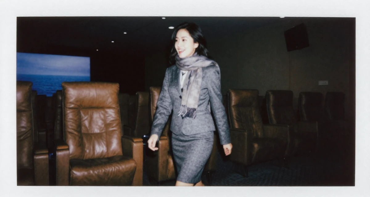 A happy Female Previously a travel-blog student, now turning trips into premium creator content in their 24, walking briskly with purpose and focus, wearing a grey wool skirt suit with a fitted jacket, wrapping a scarf around the neck in a cinema lobby.